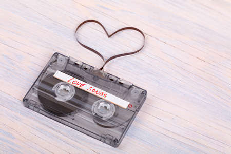 Audio cassette tape on wooden background. Audio film shaping heart, Valentine postcard. Label text love songs.の写真素材