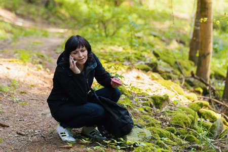 Middle age woman, on hiking trip, lost in forest, calling from mobile cell phone for help.の写真素材