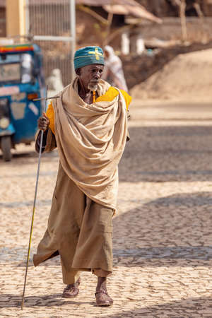 AXUM, ETHIOPIA, APRIL 27th.2019: Old man, orthodox monk or priest walk with crutch on empty street of Aksum on April 27, 2019 in Aksum, Ethiopia Africaのeditorial素材