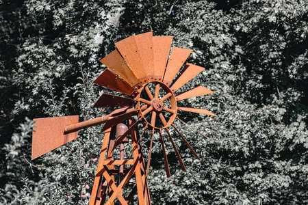 Wind powered water pump with rusty pipes on background with tree.