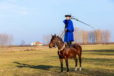 HORTOBAGY, HUNGARY, NOVEMBER, 04. 2018: Hungarian csikos in traditional folk costume showing off his trained horse. Traditional Horse-herdsman of Hungary. November 04. 2018, Hortobagy, Hungaryのeditorial素材