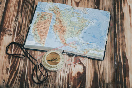 old transparent plastic sport compass with azimuth measurement on wooden background with world map atlasの写真素材