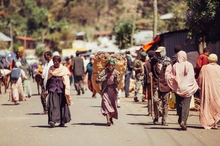 DEBRE LIBANOS, ETHIOPIA - APRIL 19, 2019: Ordinay Ethiopian woman carrying heavy bags down the street in front of Debre Libanos monastery on April 19, 2019 in Debre Libanos, Ethiopiaのeditorial素材