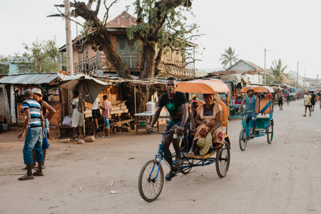 Miandrivazo, Madagascar - November 1, 2022: Traditional rickshaw bicycle with Malagasy passengers on the street, one of the ways to earn money. Everyday life on the city street of Madagascar.のeditorial素材