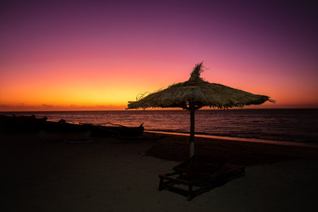 Vibrant red sky at sunset on Anakao beach in Madagascar, with a tropical parasol and sun lounger, perfect escape from everyday life.の写真素材