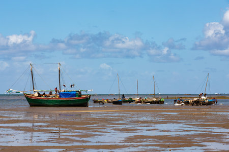 Toliara, Madagascar - November 21st 2022: Fishing boat stranded on the dry port during low tide with Malagasy people around.のeditorial素材
