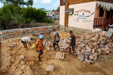 Morondava, Madagascar - November 3rd, 2022: Malagasy men working hard, manually carrying construction stones.のeditorial素材