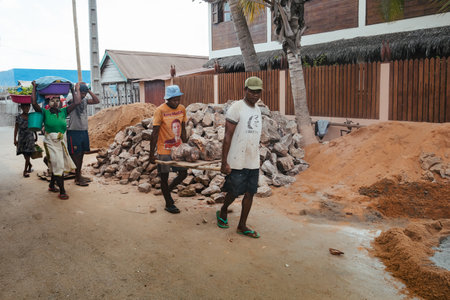 Morondava, Madagascar - November 3rd, 2022: Malagasy men working hard, manually carrying construction stones.のeditorial素材