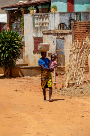 Vohitsoaka Ambalavao - November 6, 2022: Malagasy woman walking down the street with a child on her back.のeditorial素材
