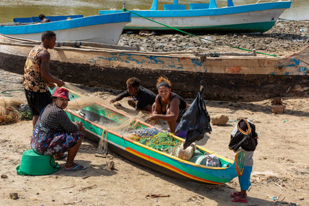 Morondava, Madagascar - November 3, 2022: Fisherman and woman repairing fishing nets at the estuaries of a river, canal Hellot. The woman has a traditionally Malagasy painted faceのeditorial素材