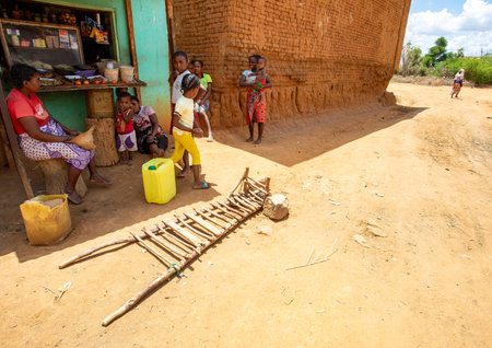 Vohitsoaka Ambalavao - November 6, 2022: Malagasy woman resting in front of market in shadow. In the foreground is a primitive wheelbarrowのeditorial素材
