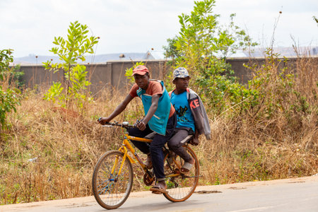 Mandoto, Madagascar - November 1st, 2022: Two Malagasy men riding a bike on a countryside road. Two Malagasy men on one bike. One leads the other.のeditorial素材