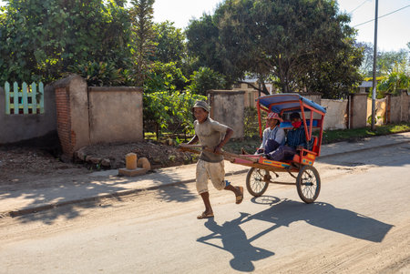 Antsirabe, Madagascar - November 2nd 2022: Rickshaw runner dashes through the crowded streets with...