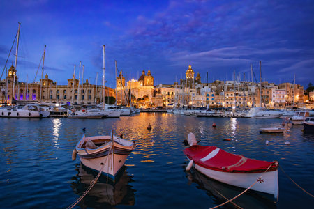 Senglea city, part of the Three Cities of Malta. Night marina glows under the night sky, yacht masts silhouetted against twinkling lights reflecting on the tranquil waters. Travel destination.の写真素材