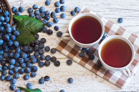 two cups of tea on a napkin  on white wooden background with blue berries blackthornの写真素材