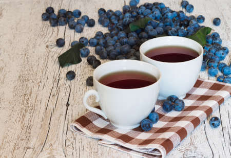 two cups of tea closeup on a napkin  on white wooden background with blue berries blackthornの写真素材