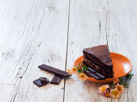 piece of chocolate cake on a plate with  chrysanthemum  and chocolate on a white wooden backgroundの写真素材