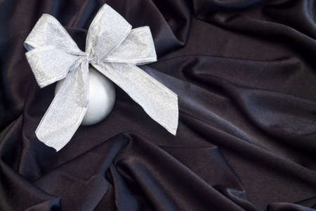 Grey Christmas ball with silver bow on black background flowing fabricの写真素材