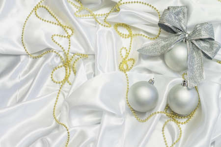 silver Christmas balls with golden beads on white satin with pleatsの写真素材