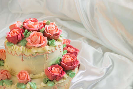 cream cake with roses closeup on a background of white satin fabricの写真素材