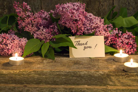 composition of a bouquet of lilac, candle and thank you card on old wooden background closeup. toned photoの写真素材