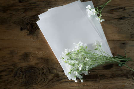 composition with a blank sheet of paper and a small bouquet of white flowers on a wooden background. Toned photoの写真素材