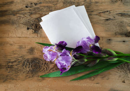 bouquet of purple iris flowers and a blank sheet of paper on a wooden backgroundの写真素材