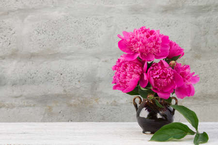 bouquet of pink peonies in a ceramic jug on a light wooden table with a blurred backgroundの写真素材