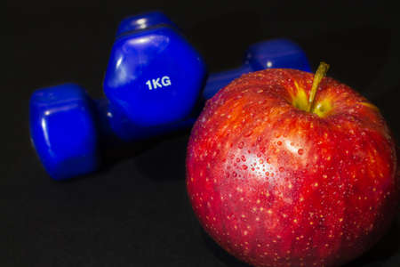 red apple with blue dumbbells on a black background. Shallow depth of fieldの写真素材