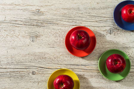 red apples on a colored saucers on a white wooden backgroundの写真素材