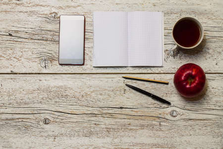 red apple with a cup of tea and a phone with an open notebook on a light wooden backgroundの写真素材