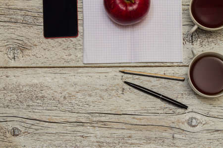 red apple with a cup of tea and a phone with an open notebook with pen closeup.  top viewの写真素材