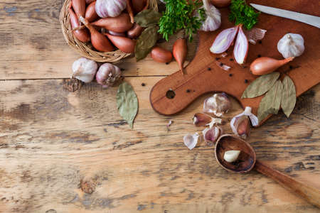 Onions with garlic heads and parsley with laurel leaves on a cutting board on a wooden background