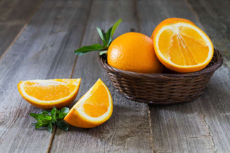 Whole and cut oranges with mint leaves close-up in a wicker basket on a wooden backgroundの写真素材