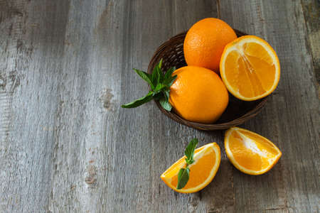 Whole and cut oranges with mint leaves close-up in a wicker basket on a wooden background. Top viewの写真素材