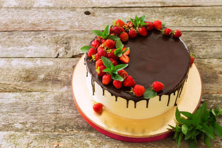 Beautiful festive cake covered with melted chocolate with strawberries and mint leavesの写真素材