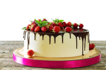 Cake decorated with strawberries and sprinkled with black chocolate on a wooden table on a white backgroundの写真素材