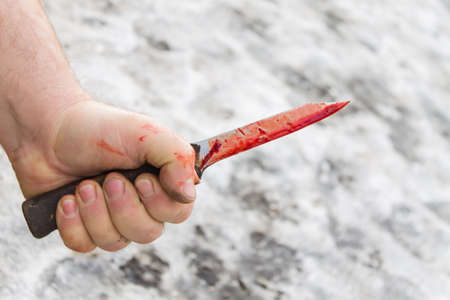 dirty mans hand with a bloody knife on the ground with snow backgroundの写真素材