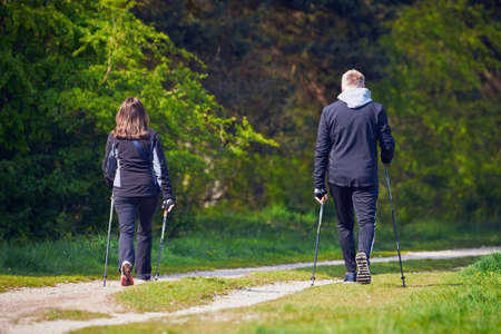 Unidentified Man and woman walking in a natural park using trekking polesの写真素材