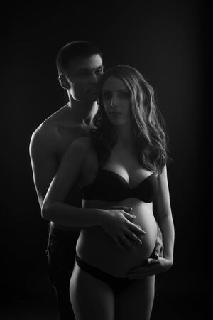 Monochrome portrait of happy loving couple in a moment of love and tenderness. Pregnant woman with hands over tummy. Black and white photoの写真素材
