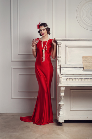 Young beautiful girl in red dress style of the 20's or 30's with glass of martini near the piano....
