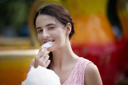 Cute caucasian girl in amusement park is eating pink candyfloss. Portrait of happy attractive young woman with cotton candyの写真素材