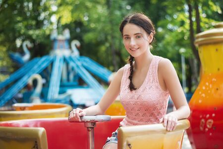 Attractive happy smiling girl in an amusement park sitting on carouselの写真素材