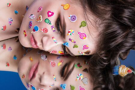 Beautiful fashion girl with luxury professional makeup and funny emoji stickers glued on the face. Young woman with cupcake in handsの写真素材