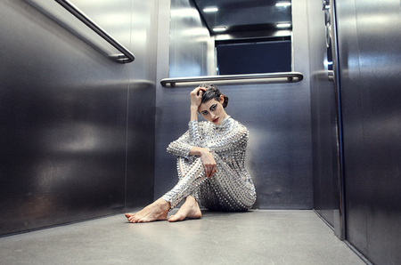 Young cyber woman in silver futuristic costume sitting in the elevatorの写真素材
