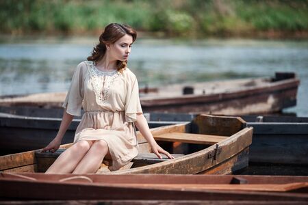 Portrait of pretty young woman sitting in the boat on river bankの写真素材
