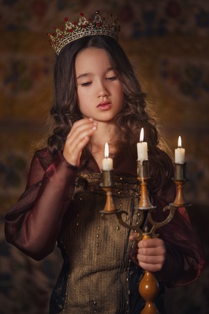 Portrait of cute girl wearing a crown with candlestick in hands. Young queen or princessの写真素材