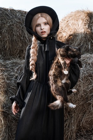 Fashion young woman wearing stylish black dress and hat at countryside. Amish fashion styleの写真素材