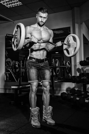 Athletic young man doing exercises with barbell in gym. Handsome muscular bodybuilder guy is working out. Monochrome imageの写真素材