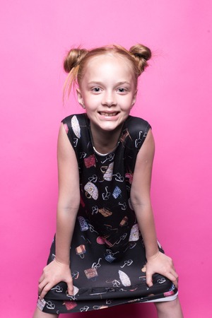 Beautiful little redhead girl in dress posing like model on pink backgroundの写真素材